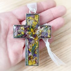 a hand holding a small cross with flowers on it's side and white ribbon around the edge