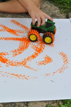 a child is drawing with orange paint on a sheet of paper that has a tractor drawn on it