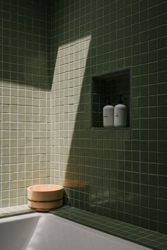 a green tiled bathroom with a white bathtub and wooden bowl on the counter next to it