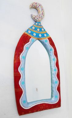 a decorative mirror hanging on the side of a white wall with a blue and red design