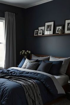 a bedroom with dark blue walls and white bedding, framed pictures on the wall