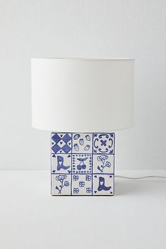 a blue and white table lamp with a square shade on the top, sitting against a wall