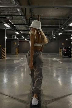 a woman in a white hat and grey sweatpants is walking through an empty parking garage