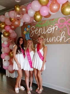 three girls in white dresses and pink sashes posing for the camera with balloons behind them