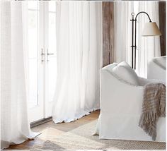 a white couch sitting in front of a window covered in sheer curtains and a blanket