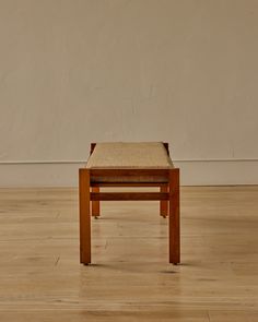 a small wooden stool sitting on top of a hard wood floor next to a white wall