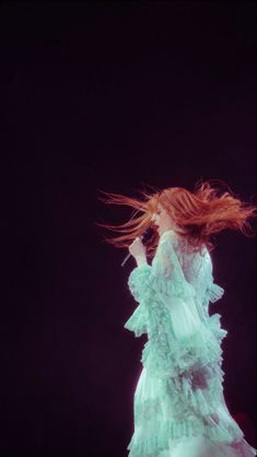 a woman in a green dress with her hair blowing in the wind, on stage