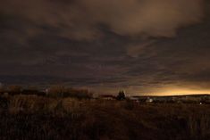 the night sky is dark and cloudy over a field with houses in the foreground