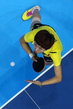 a woman holding a ping pong racket on top of a blue tennis court