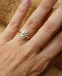 a woman's hand with a diamond ring on top of her finger and a piece of wood in the background