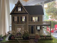 a doll house is on display in front of a window with flowers and greenery