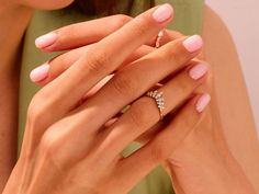 a woman with pink nails holding onto her wedding band and engagement ring in front of her face