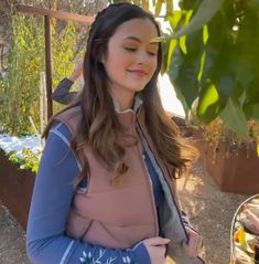 a woman standing next to a potted plant and looking at the camera with her eyes closed