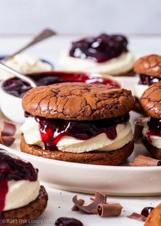 two dessert sandwiches with whipped cream and blueberry sauce on them, sitting on a white plate