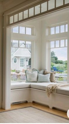 a window seat with pillows on it in front of two large windows and a rug