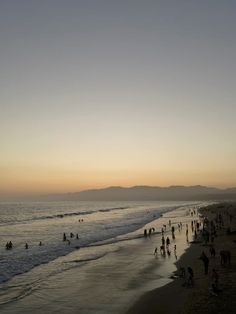 many people are walking on the beach at sunset