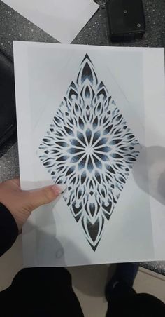 someone holding up a piece of paper with an intricate design on it