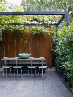 an outdoor dining table surrounded by greenery and shrubbery in the back yard area