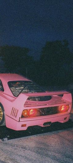 a pink sports car parked on the side of the road at night with it's hood up