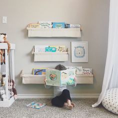 a person sitting on the floor reading a book next to a crib with stuffed animals