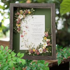 a wooden frame with paper flowers and greenery around it on top of a table