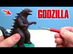 someone is holding a toy godzilla with a marker in their hand and pointing to it