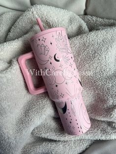 a pink travel mug with stars and moon designs on it sitting on a bed next to a white blanket