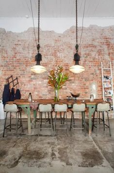 a dining room table and chairs in front of a brick wall with hanging lights above it