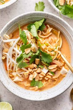 two bowls filled with soup and garnished with cilantro, peanuts, lime leaves