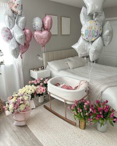 a baby in a crib with balloons and flowers on the floor next to it