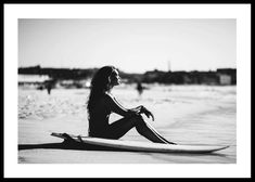 a black and white photo of a woman sitting on a surfboard in the sand