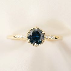 an engagement ring with a blue sapphire and diamonds on it's sidestone, sitting on a white cloth