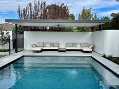 a swimming pool with lounge chairs next to it and a white fence in the background