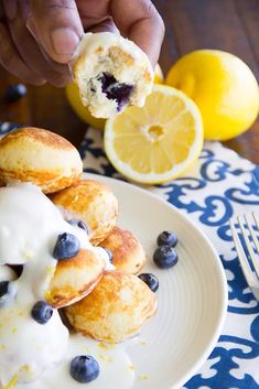 a person holding a pastry with blueberries and lemons in the background on a plate