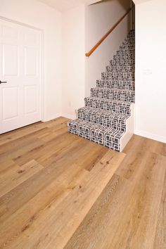 an empty room with wooden floors and stairs leading up to the second floor, in front of a white door