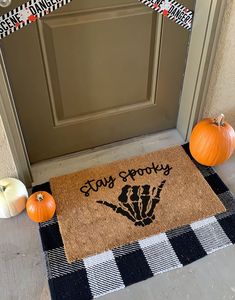 two pumpkins are sitting on the front door mat next to an entrancemat that says, stay spooky