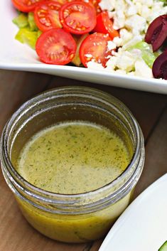 there is a jar of dressing next to a plate with salad and vegetables on it