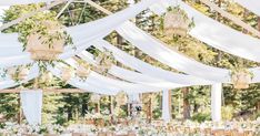 an outdoor wedding reception with white draping and greenery hanging from the ceiling