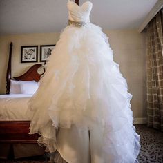 a wedding dress is displayed on a mannequin in front of a bed with curtains