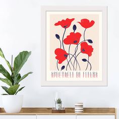 an art print with red poppies on a white wall above a wooden cabinet and plant