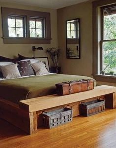 a large bed sitting next to a window on top of a hard wood floor covered in pillows