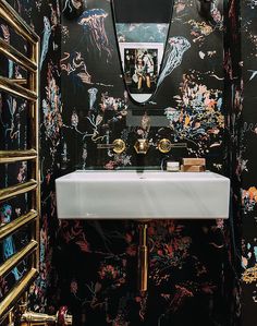 a bathroom with black and gold wallpaper, a white sink and mirror on the wall