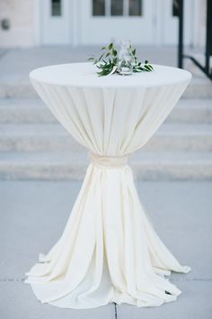 a table with white cloth draped over it and some flowers on the top, sitting in front of steps