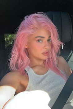 a woman with pink hair sitting in the back seat of a car looking at the camera