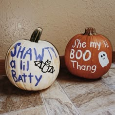 two painted pumpkins sitting side by side on the ground with words written on them