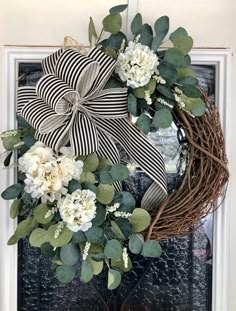 a wreath with white flowers and greenery is hanging on the side of a door