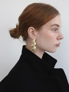 a woman with red hair wearing large gold earring on her head and black coat