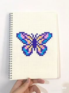 a hand holding a notebook with a cross stitch butterfly on it