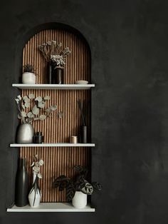 three white shelves with vases and flowers on them against a black wall in an otherwise dark room