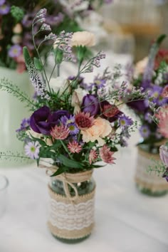 three vases filled with flowers sitting on top of a white tablecloth covered table